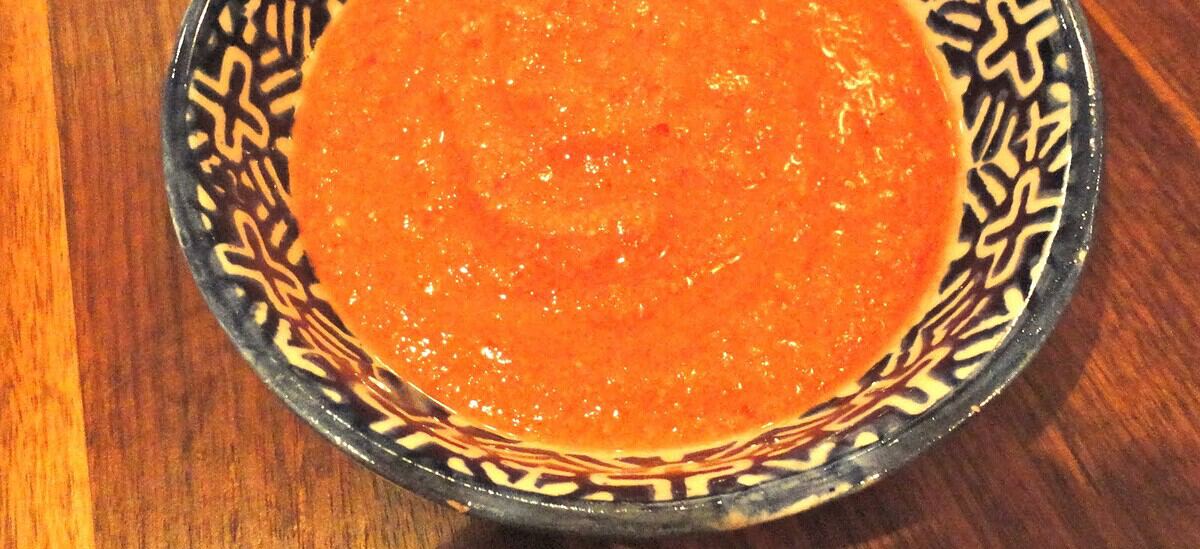 Orange sauce in a blue patterned bowl on a wooden table, close-up.