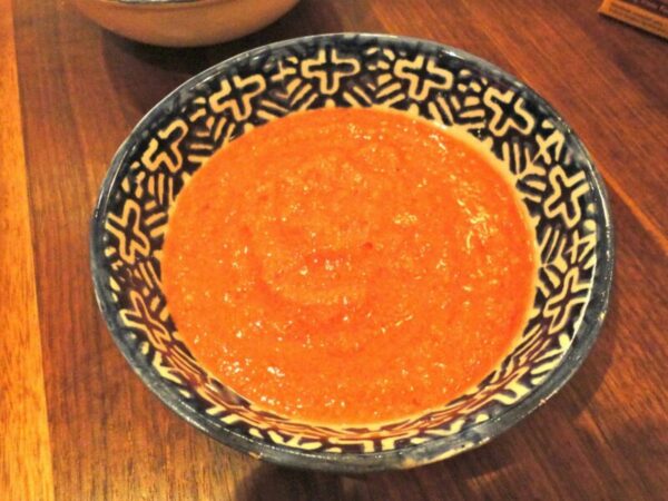 Orange sauce in a blue patterned bowl on a wooden table, close-up.