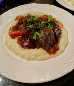 A beef and carrot stew is topped with parsley and served on a bed of mashed potatoes