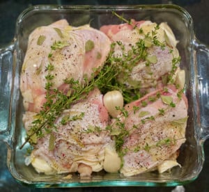Four uncooked Chicken thighs in Pyrex dish with herbs and garlic tucked around the thighs