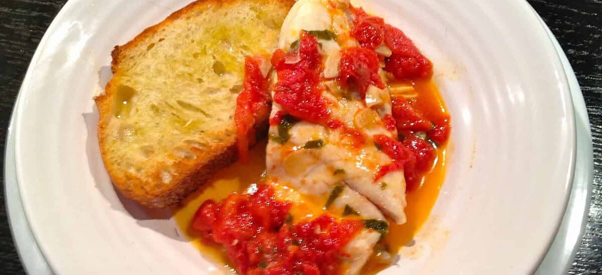 Plate with chicken in tomato‑herb sauce and a slice of toasted bread on the side.