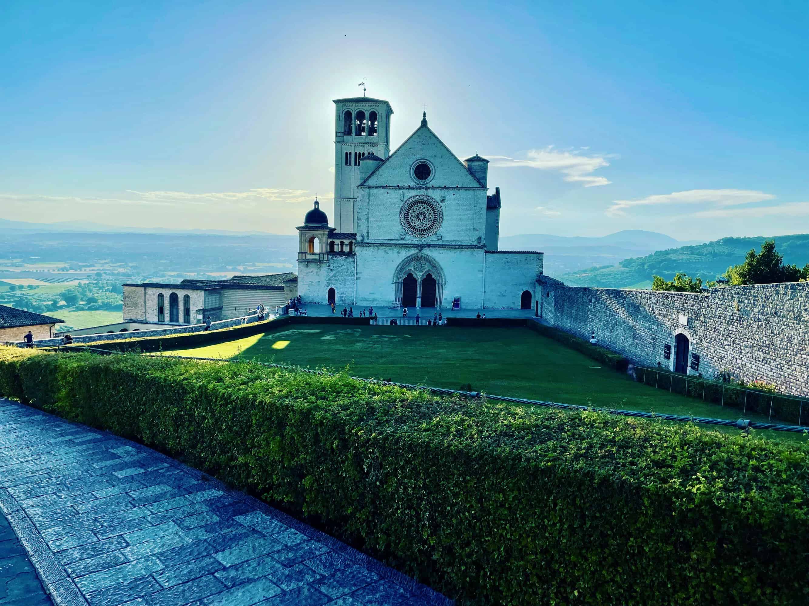 Front view of a historic stone church with a large circular rose window and tall bell tower, set on a hill with manicured lawn and clear blue sky.