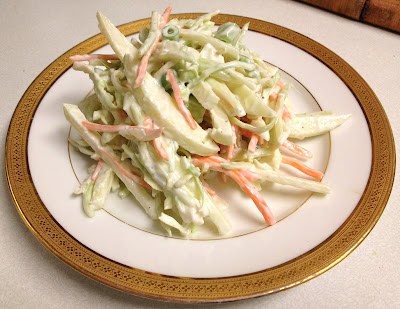 Creamy coleslaw with shredded cabbage and carrot on a decorative plate with a gold rim, served on a light countertop.