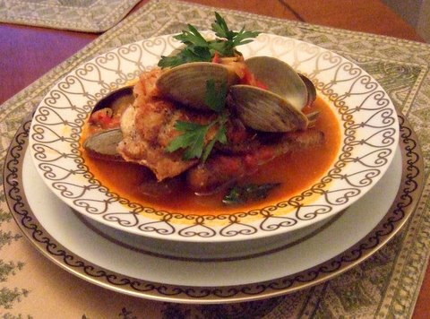 Dish of fried fish fillet in tomato-based sauce with clams, garnished with parsley on an ornate plate, ready to serve