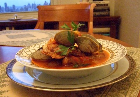 Clams in tomato sauce garnished with parsley served on a decorative plate at a dining table.