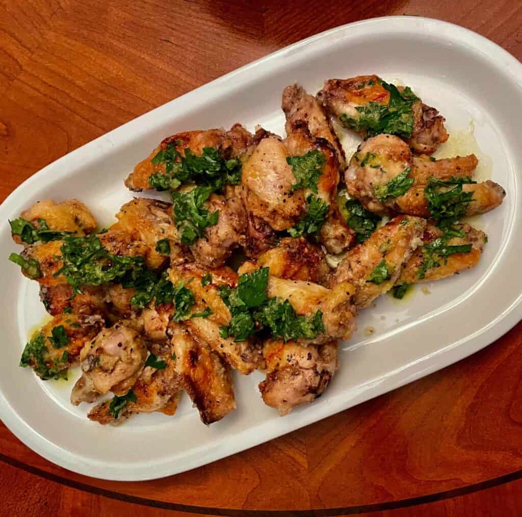 Cooked chicken pieces on a white plate garnished with chopped parsley, served on a wooden table