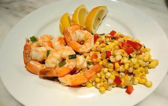Plate with shrimp, lemon wedges, and a colorful corn-pepper relish on a white dish.