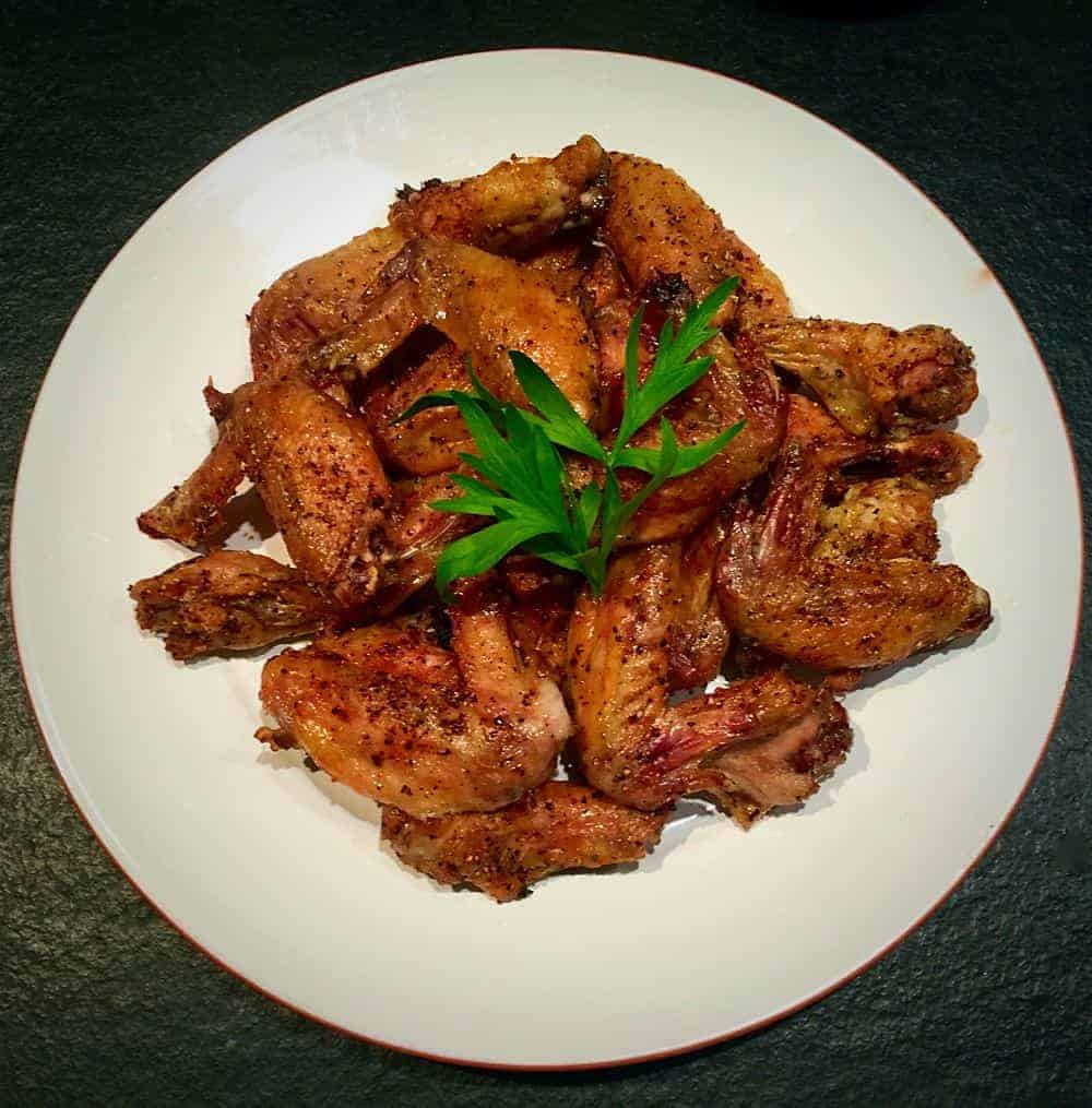 Plate of crispy seasoned chicken wings arranged on a white dish, garnished with a sprig of parsley
