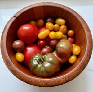 Wooden bowl filled with colorful cherry tomatoes on a light surface.