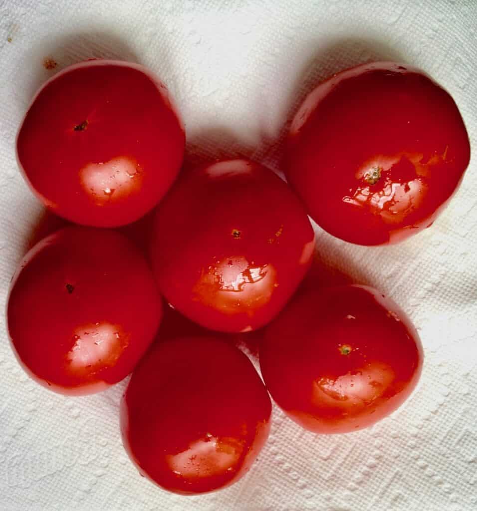 Six small red tomatoes resting on a white textured cloth.