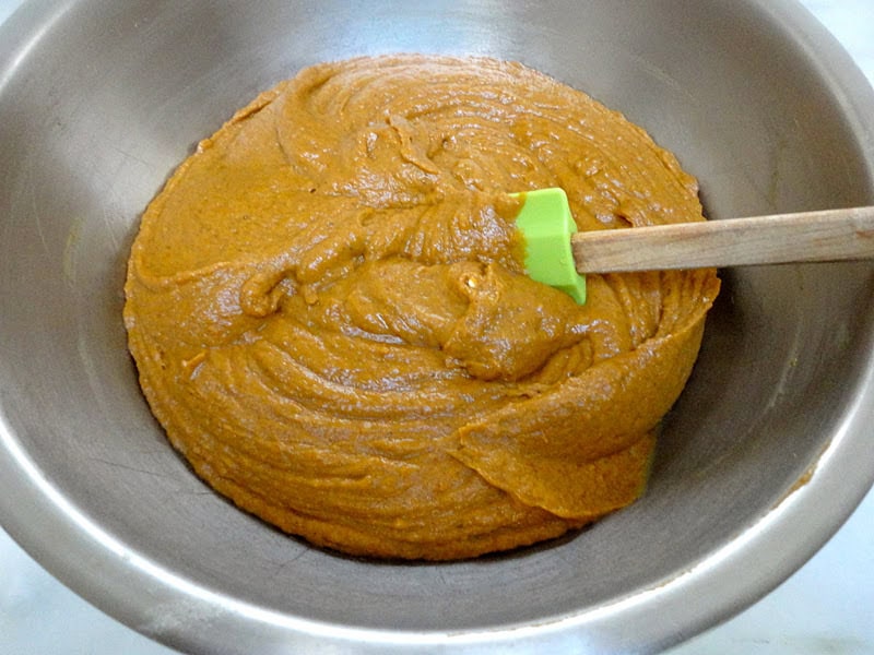 Orange pumpkin whoopie pie batter in a metal mixing bowl with a green spatula.