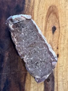 Oven-cooked shell steak with an unbrowned grey surface on a wooden cutting board.