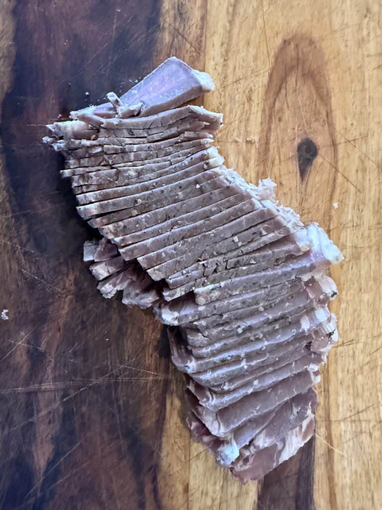 Cooked steak cut into thin slices on a wooden cutting board.