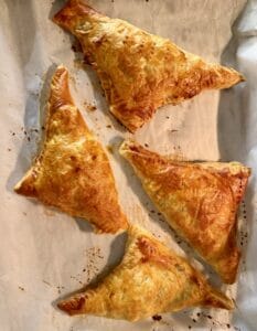 Four baked triangular puff-pastry turnovers on a parchment-lined baking sheet.
