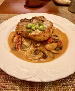 Seared pork chop served over sliced mushrooms and cherry tomatoes in a creamy pistachio sauce.