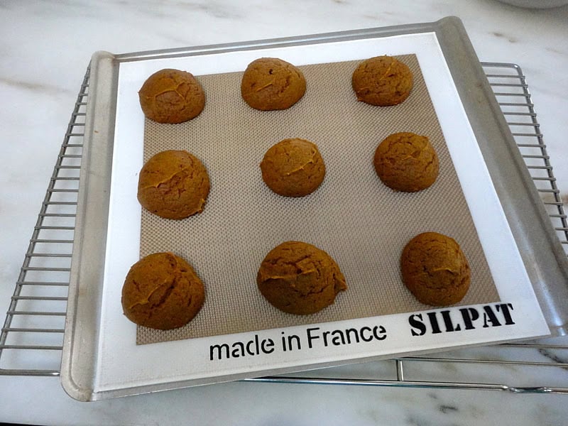 Nine baked pumpkin cookies on a silicone-lined baking sheet.